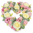 A tender heart-shaped wreath of pastel flowers is captured against a stark white background, the clean setting enhancing the softness of the design. The heart is absolutely full, leaving no gaps, so the flowers appear to flow seamlessly into one another. Cream and pale yellow roses rise gently from the surface, their layered petals swirling inward to form graceful, rounded blooms that lend an air of classic elegance. Around them, clusters of soft pink carnations create a richly textured base, each frilled petal catching light and shadow so that the overall effect is one of delicate movement. Deeper shades of pink and mauve lisianthus blooms are dotted through the arrangement, their open, cup-like flowers drawing the eye deeper into the heart, as though inviting quiet reflection. Woven among the petals are strands of eucalyptus foliage, the silvery-green leaves lying delicately along the contours of the heart, cooling the palette and framing the design with natural grace. Tiny yellow-green buds are scattered throughout, adding hints of new life and a sense that the wreath has been freshly made by a thoughtful Poplar florist familiar with local families and their traditions. The mood of the piece is gentle and consoling, perfect for funeral services, cremations, or memorial gatherings in Poplar and nearby Limehouse or Canary Wharf, where loved ones come together to honour a life. This floral heart feels like a soft-spoken message of remembrance and love, offering visual comfort and a touch of beauty at a time when it is most needed.